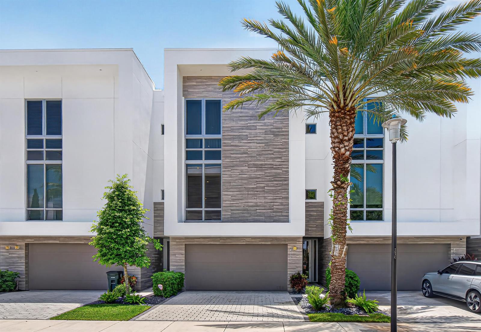 A modern three-story townhouse exterior features white walls, wood-look siding, and a palm tree — 4130 NW 17th Avenue, Boca Raton FL 33431, BOCA RATON, FL