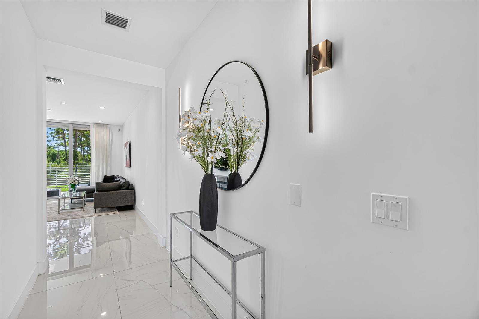 A modern hallway features a glass console table, a round mirror, and white tile flooring — 4130 NW 17th Avenue, Boca Raton FL 33431, BOCA RATON, FL