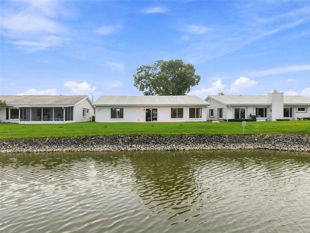 A row of white single-story houses sits behind a rocky bank along a lake — 3555 93RD AVENUE N UNIT 6, PINELLAS PARK, FL