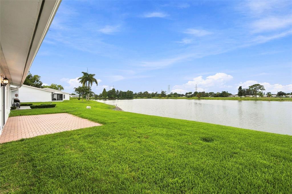 A paved patio overlooks a grassy lawn and a large pond behind a residential house — 3555 93RD AVENUE N UNIT 6, PINELLAS PARK, FL