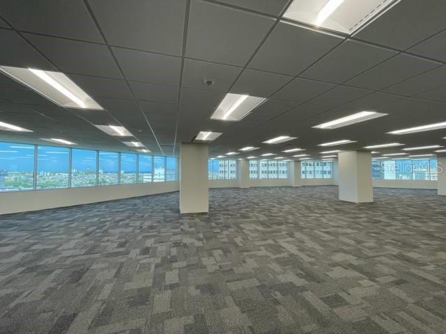 An empty office space features gray patterned carpeting, a drop ceiling, and floor-to-ceiling windows — 250 MUÑOZ RIVERA, SAN JUAN, PR