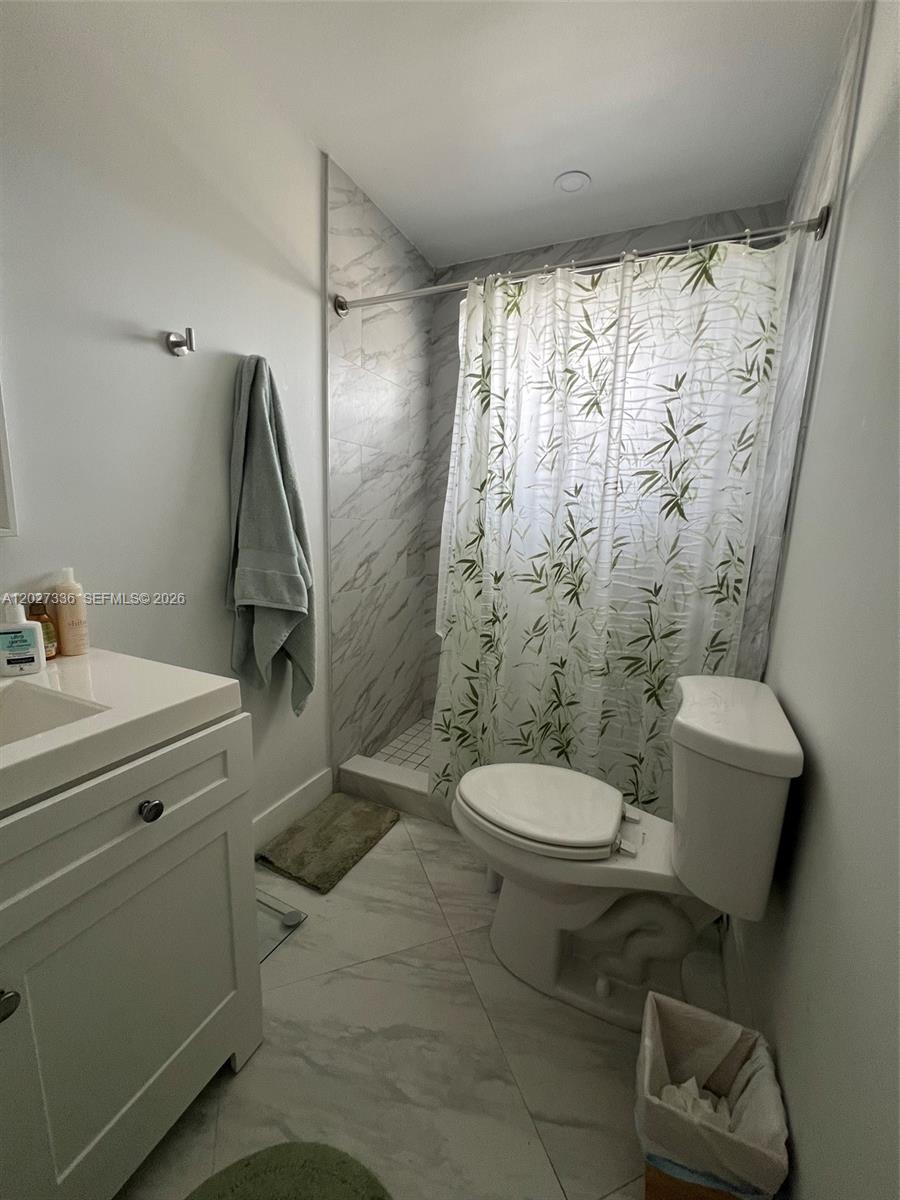 A bathroom features a white vanity, a toilet, and a tiled shower with a bamboo-patterned curtain — 1000 NE 14th Ave # 408, Hallandale Beach FL 33009, HALLANDALE BEACH, FL
