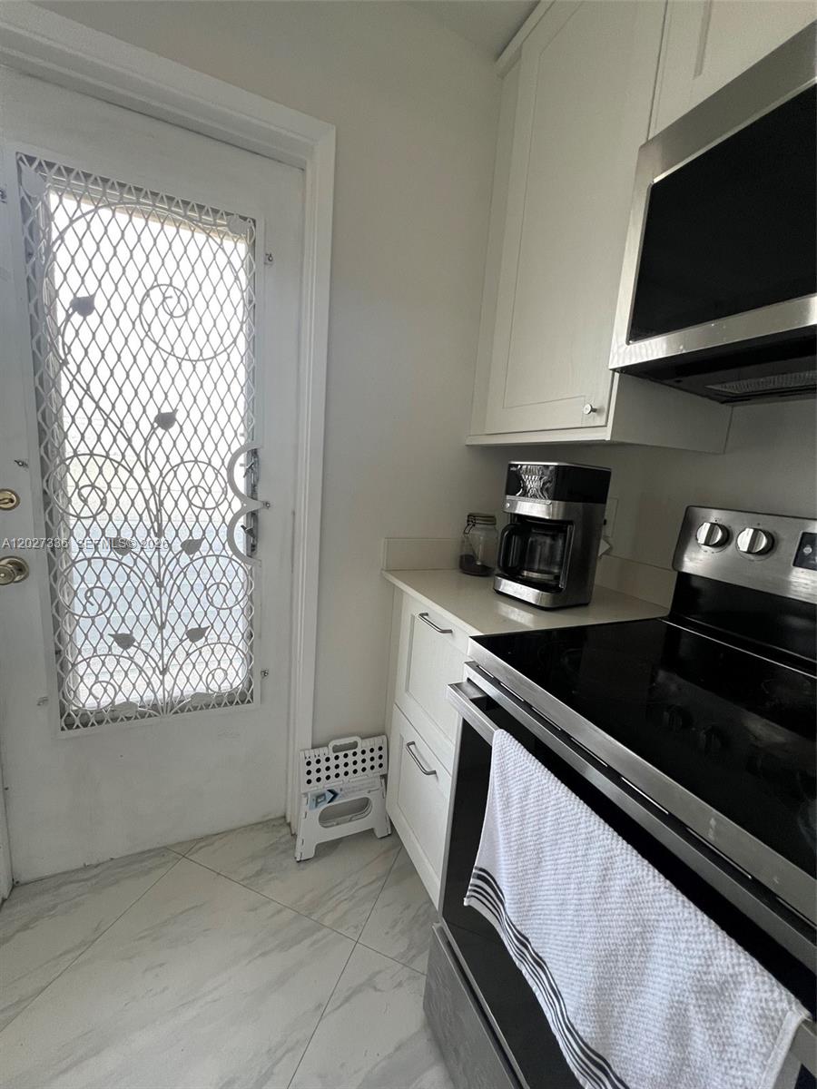 A kitchen features white cabinets, a stainless steel stove, a coffee maker, and a screen door — 1000 NE 14th Ave # 408, Hallandale Beach FL 33009, HALLANDALE BEACH, FL