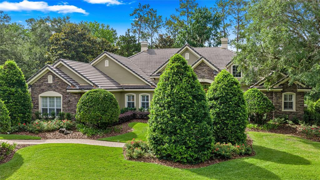 A tan stucco and stone house with a dark tile roof and manicured landscaping — 3135 NW 79TH AVENUE ROAD, OCALA, FL