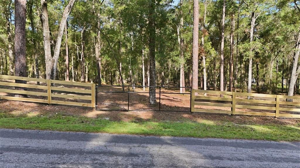 A wooden fence with a central metal gate borders a wooded lot along a road — 5230 S ROBERT BLAKE AVENUE, INVERNESS, FL