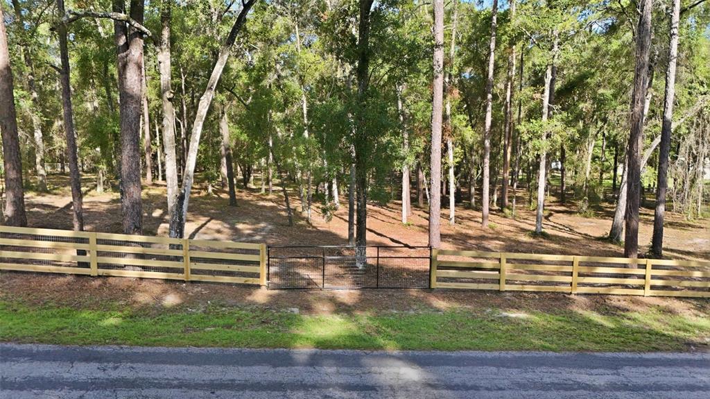 A wooden fence with a central metal gate borders a wooded lot along a road — 5230 S ROBERT BLAKE AVENUE, INVERNESS, FL
