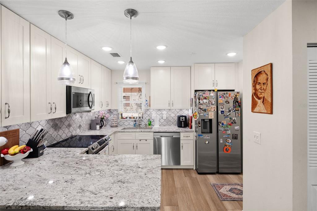 A kitchen with white cabinets, granite countertops, stainless steel appliances, and a patterned tile backsplash — 5400 34TH STREET W UNIT I3, BRADENTON, FL