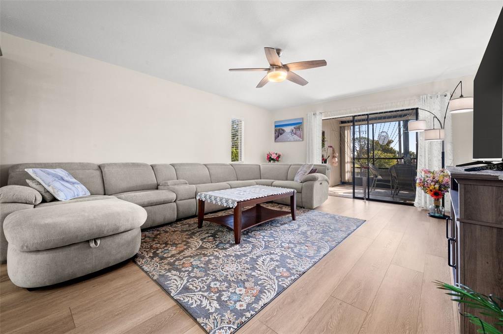 A living room features a large gray sectional sofa, a patterned rug, and sliding glass doors — 5400 34TH STREET W UNIT I3, BRADENTON, FL