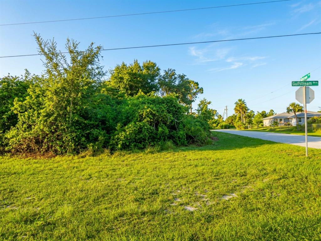 A grassy vacant lot with dense vegetation sits at a street corner with signage — 12303 GULFSTREAM BOULEVARD, PORT CHARLOTTE, FL
