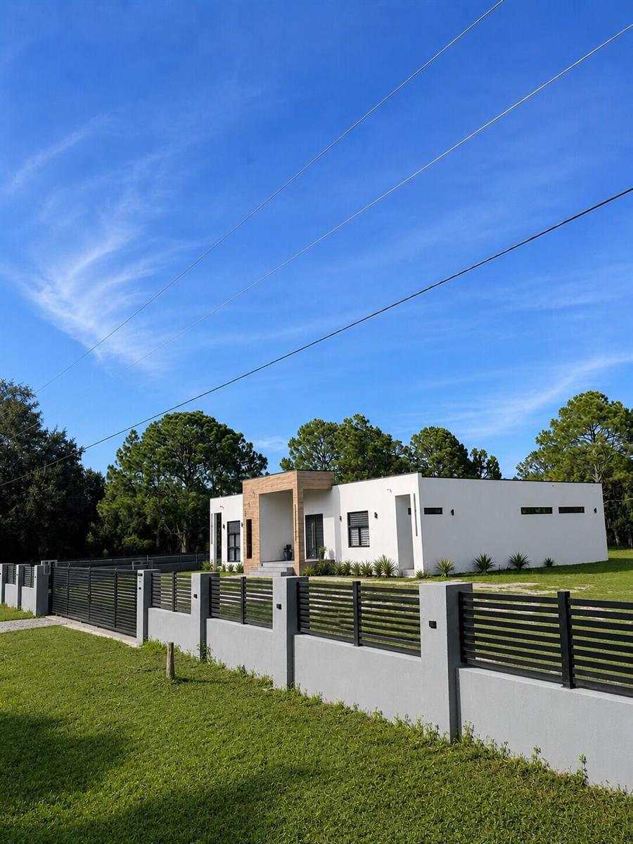 A modern white house with a wood-accented entryway sits behind a contemporary metal fence — 345 N Jinete Street, Clewiston FL 33440, CLEWISTON, FL