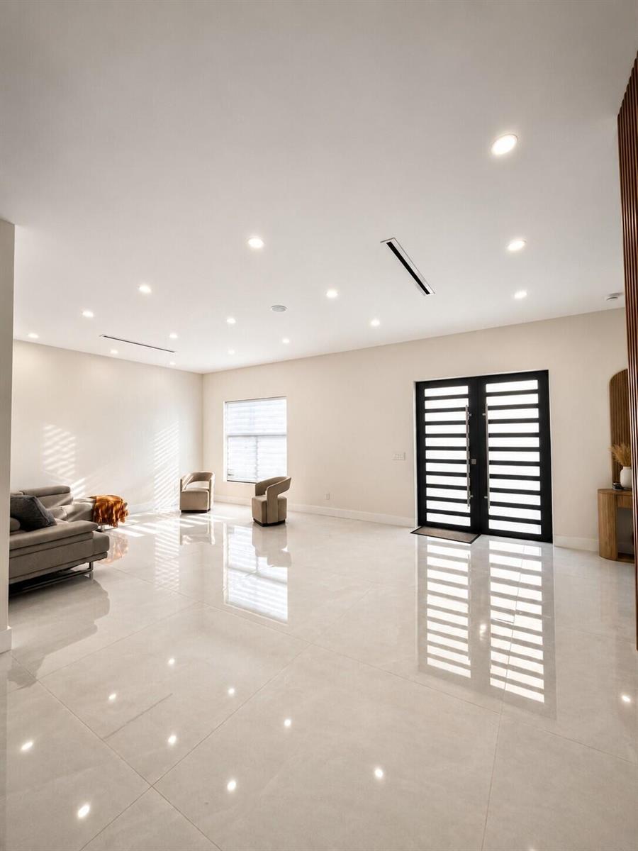 A spacious living room features glossy tile flooring, recessed lighting, and a modern black-framed door — 345 N Jinete Street, Clewiston FL 33440, CLEWISTON, FL