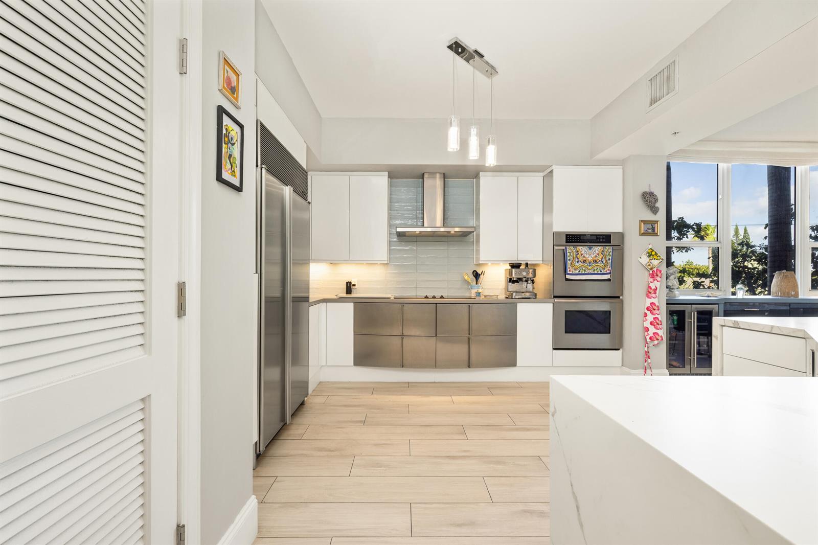 A modern kitchen features white upper cabinets, stainless steel lower cabinets, and a large refrigerator — 701 SE 21st Avenue # 201, Deerfield Beach FL 33441, DEERFIELD BEACH, FL
