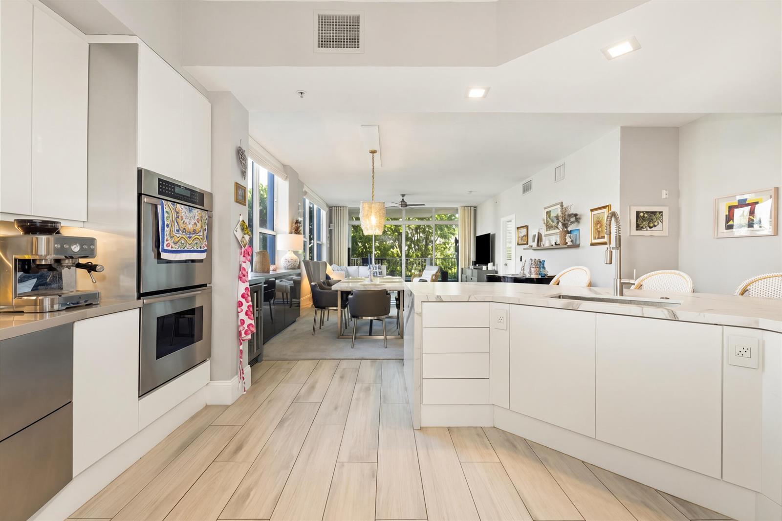 A modern kitchen with white cabinetry and a marble island opens into a dining area — 701 SE 21st Avenue # 201, Deerfield Beach FL 33441, DEERFIELD BEACH, FL