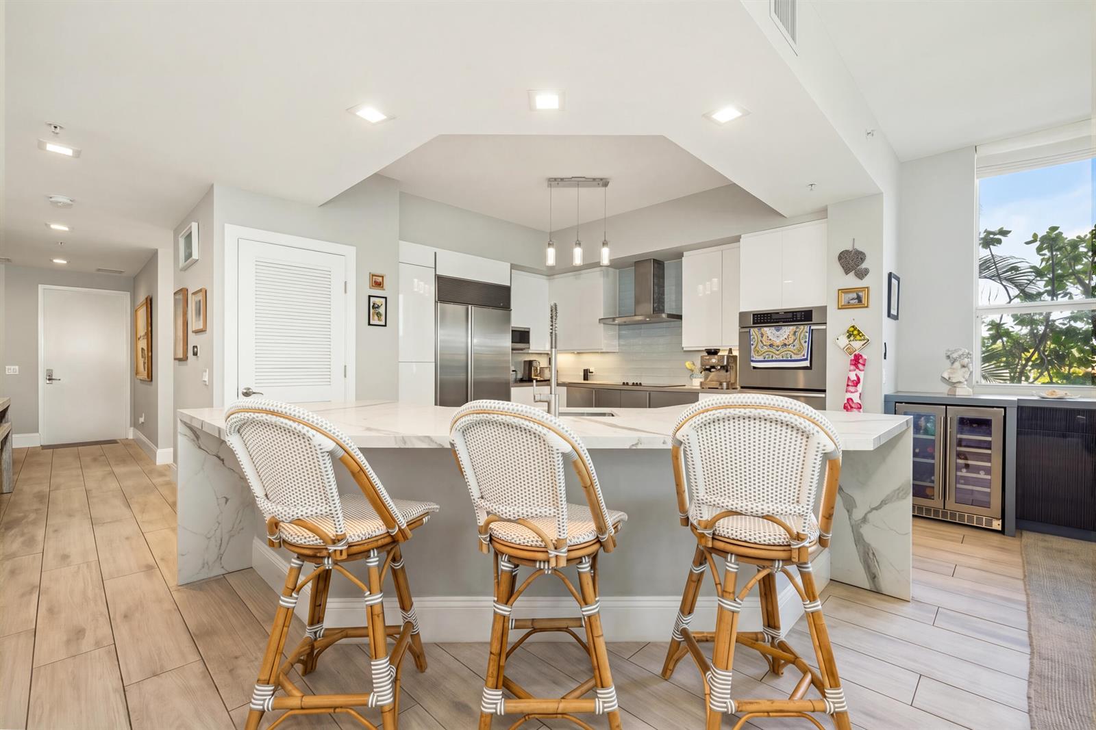 A modern kitchen features a marble-topped island with three rattan bar stools and stainless appliances — 701 SE 21st Avenue # 201, Deerfield Beach FL 33441, DEERFIELD BEACH, FL