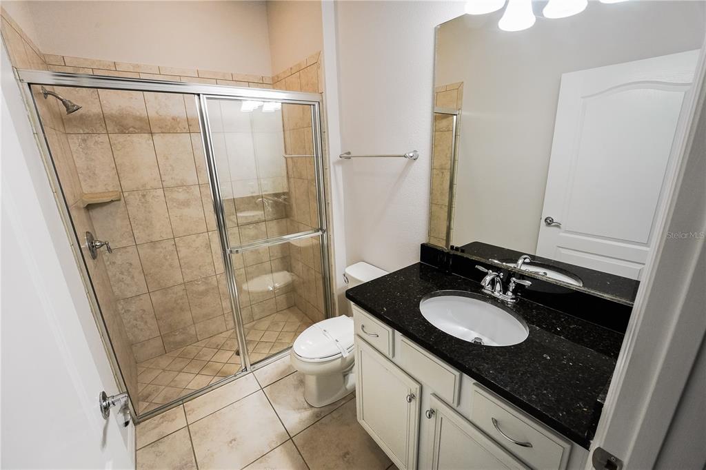 A bathroom features a tiled walk-in shower, a toilet, and a vanity with dark countertops — 1885 GOBI DRIVE, KISSIMMEE, FL
