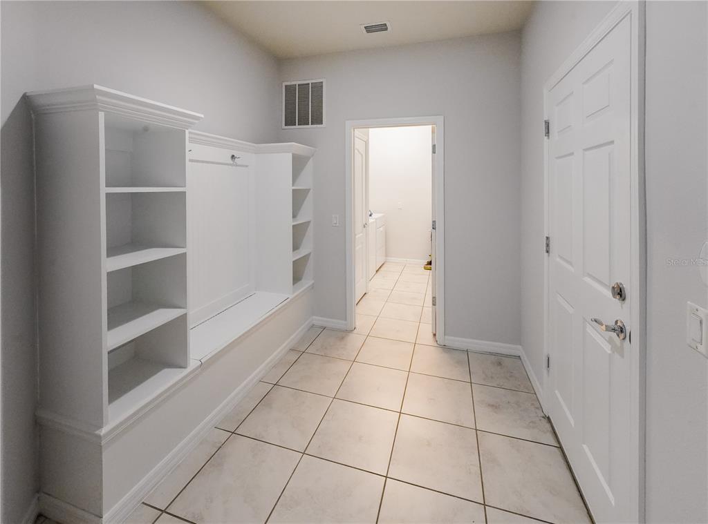 A mudroom features white built-in shelving, a bench, tile flooring, and a doorway to laundry — 1885 GOBI DRIVE, KISSIMMEE, FL