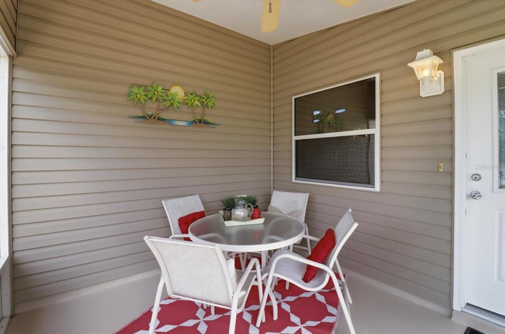A covered patio features a glass-top table with four chairs on a red patterned rug — 2348 RILEY ROAD, THE VILLAGES, FL