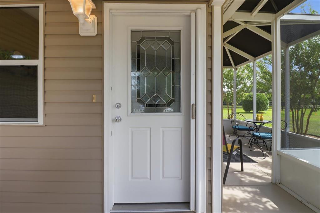 A white front door with a decorative glass insert sits beside a screened-in porch — 2348 RILEY ROAD, THE VILLAGES, FL