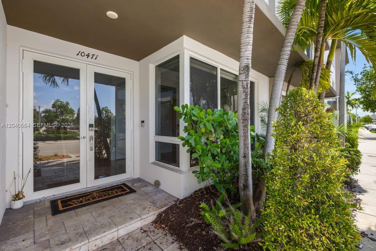 The exterior entrance features double glass doors, a welcome mat, and surrounding tropical landscaping — 10471 NW 66th St, Doral FL 33178, DORAL, FL