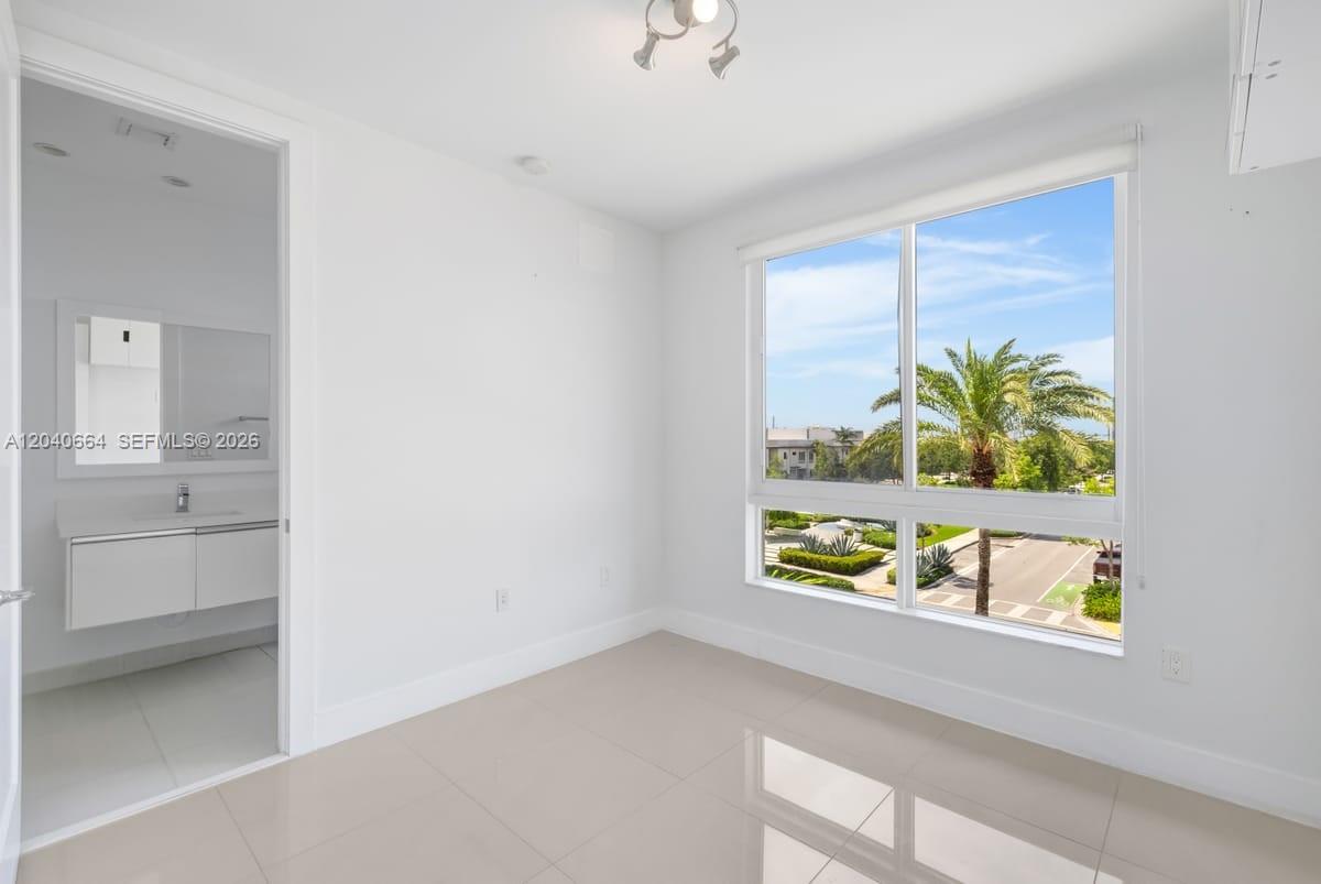 A bright, empty room with white walls, tile flooring, and a large window overlooking palm trees — 10471 NW 66th St, Doral FL 33178, DORAL, FL