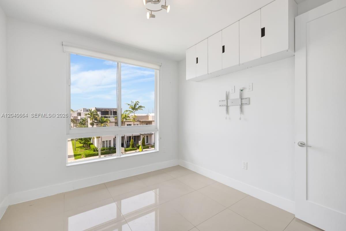 A bright room features white walls, tile flooring, overhead storage cabinets, and a large window — 10471 NW 66th St, Doral FL 33178, DORAL, FL