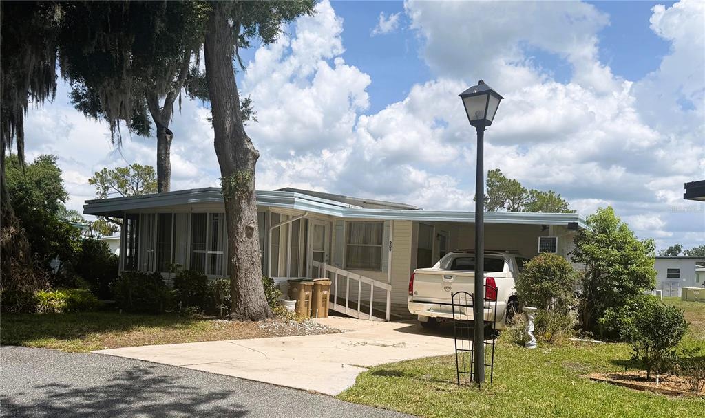 A single-story manufactured home with a carport, a wheelchair ramp, and a tall lamp post — 209 JACARANDA DRIVE, LEESBURG, FL