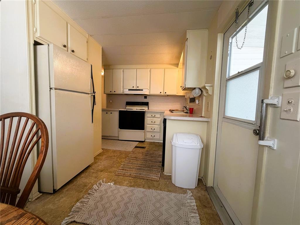 A kitchen features white cabinets, a white refrigerator, a stove, and a white trash can — 209 JACARANDA DRIVE, LEESBURG, FL