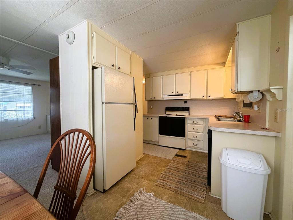A kitchen features white cabinets, a white refrigerator, a stove, and light-colored countertops — 209 JACARANDA DRIVE, LEESBURG, FL