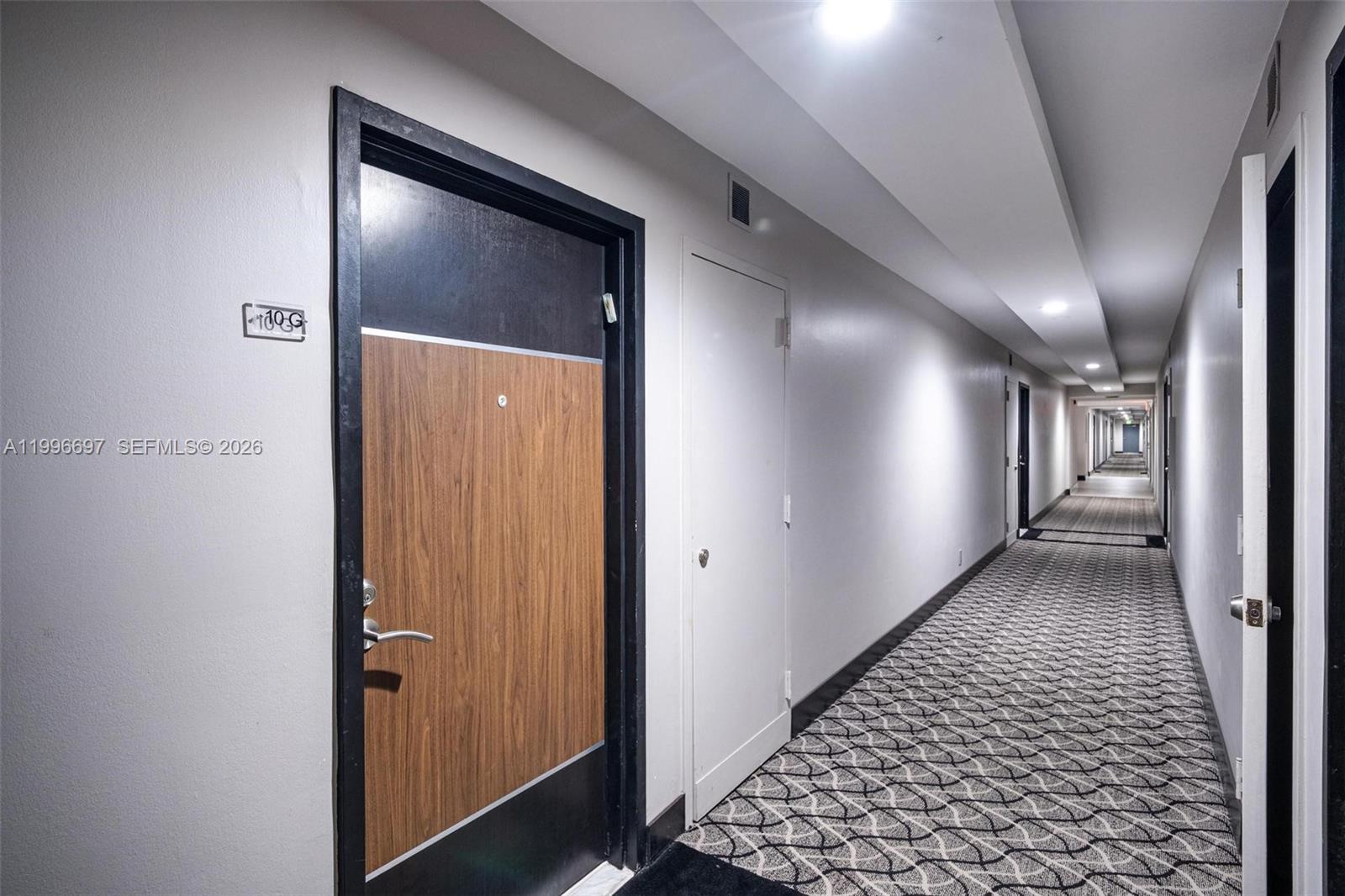 A long apartment hallway features patterned carpeting, white walls, and several closed doors — 1500 S Ocean Dr # G10, Hollywood FL 33019, HOLLYWOOD, FL