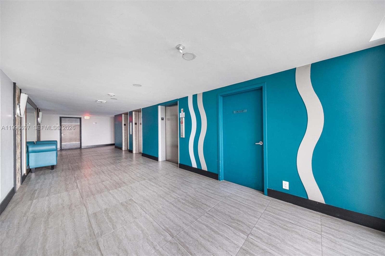 A hallway features teal walls with white wave accents, tile flooring, and elevator doors — 1500 S Ocean Dr # G10, Hollywood FL 33019, HOLLYWOOD, FL