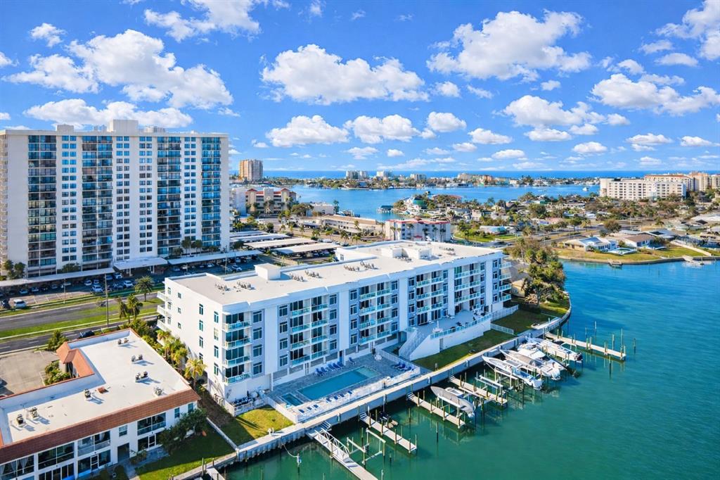 An aerial view shows a white waterfront apartment building with a pool and boat docks — 415 ISLAND WAY UNIT 402, CLEARWATER BEACH, FL