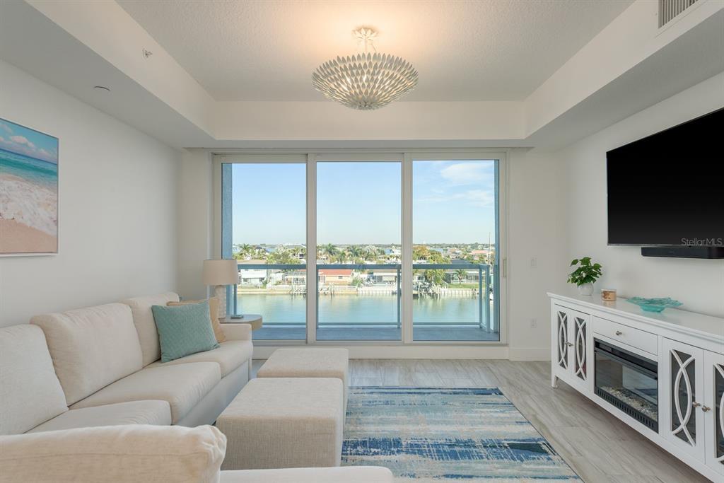 A living room with a white sofa, fireplace console, and sliding doors overlooking a waterway — 415 ISLAND WAY UNIT 402, CLEARWATER BEACH, FL