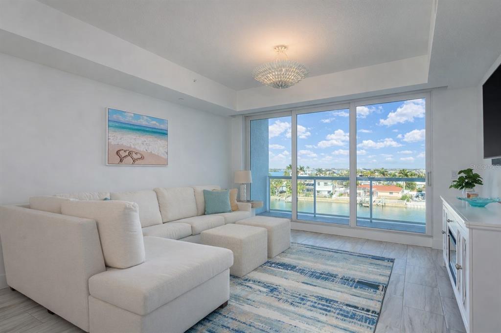 A bright living room features a white sectional sofa, a blue rug, and floor-to-ceiling windows — 415 ISLAND WAY UNIT 402, CLEARWATER BEACH, FL
