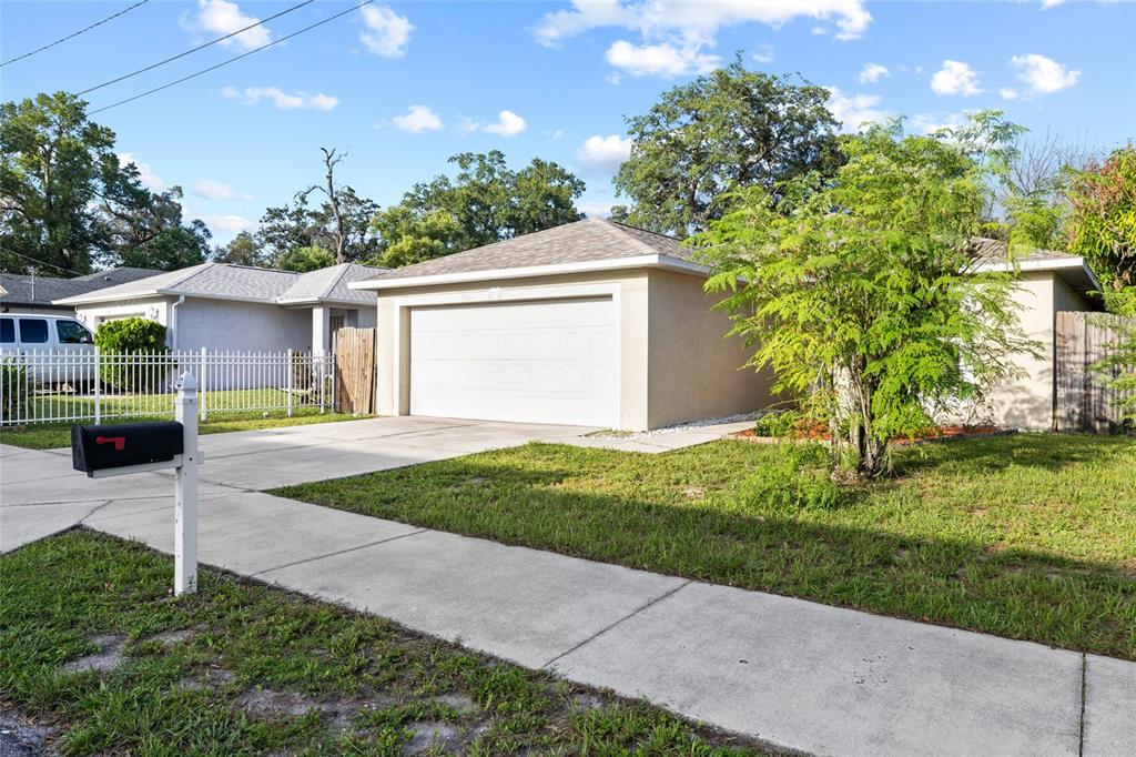 A single-story house with a white garage door, a concrete driveway, and a front lawn — 10001 FLORENCE AVENUE N, TAMPA, FL