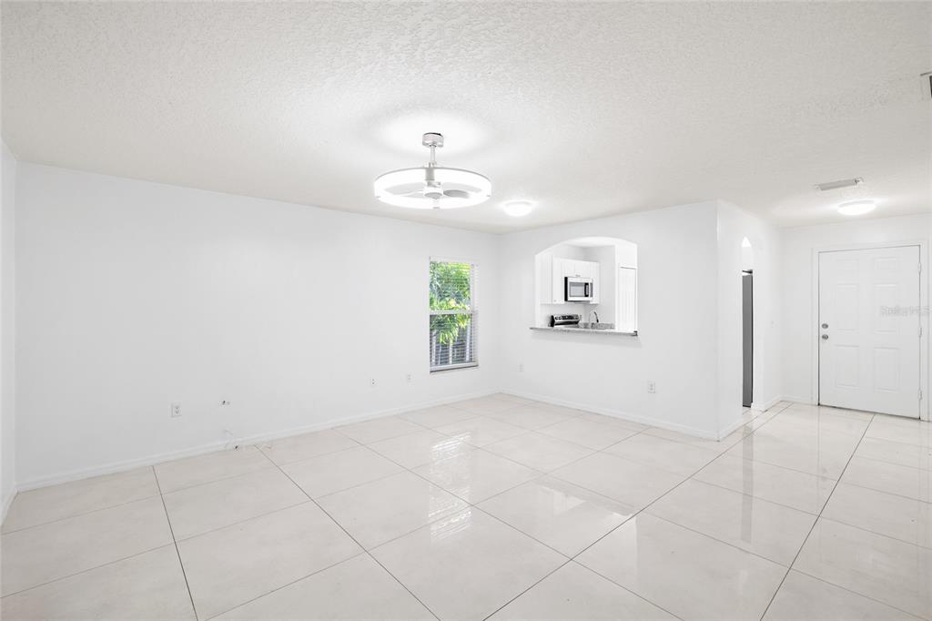An open-concept living area features white tile flooring, a ceiling fan, and a kitchen pass-through — 10001 FLORENCE AVENUE N, TAMPA, FL