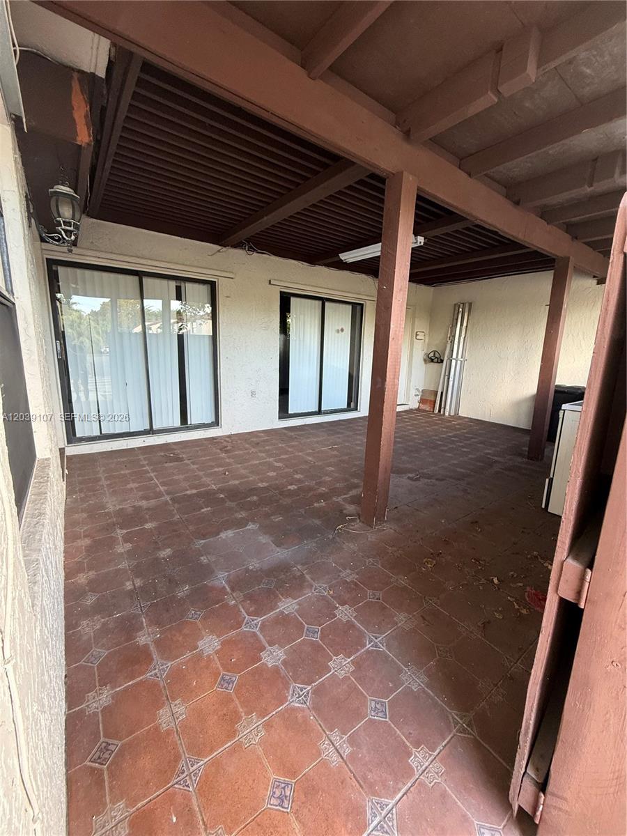 A covered patio features brown tiled flooring, wooden support beams, and two sliding glass doors — 9700 NW 6th Ln # 9700, Miami FL 33172, MIAMI, FL