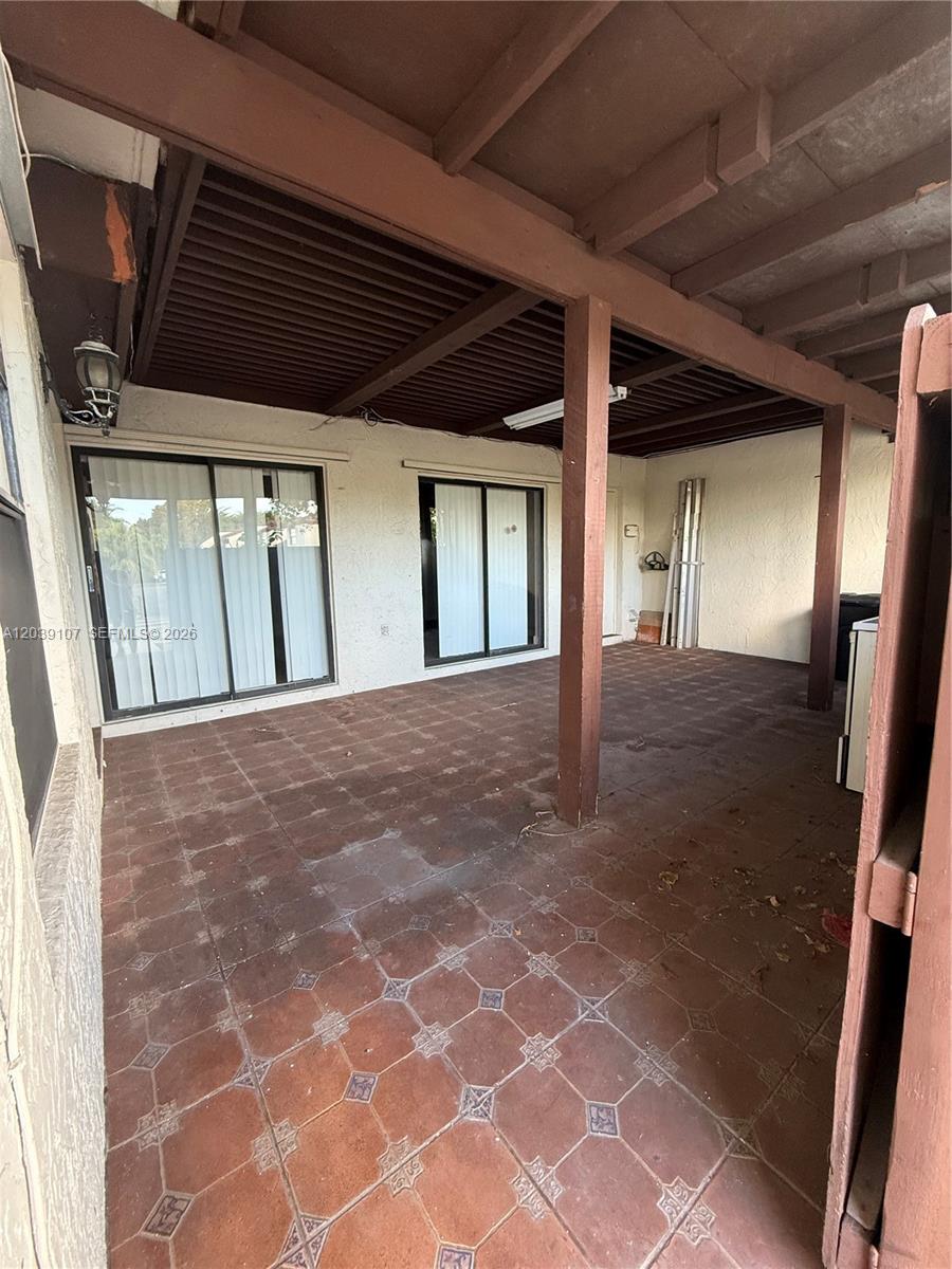 A covered patio features brown tiled flooring, wooden support beams, and two sliding glass doors — 9700 NW 6th Ln # 9700, Miami FL 33172, MIAMI, FL