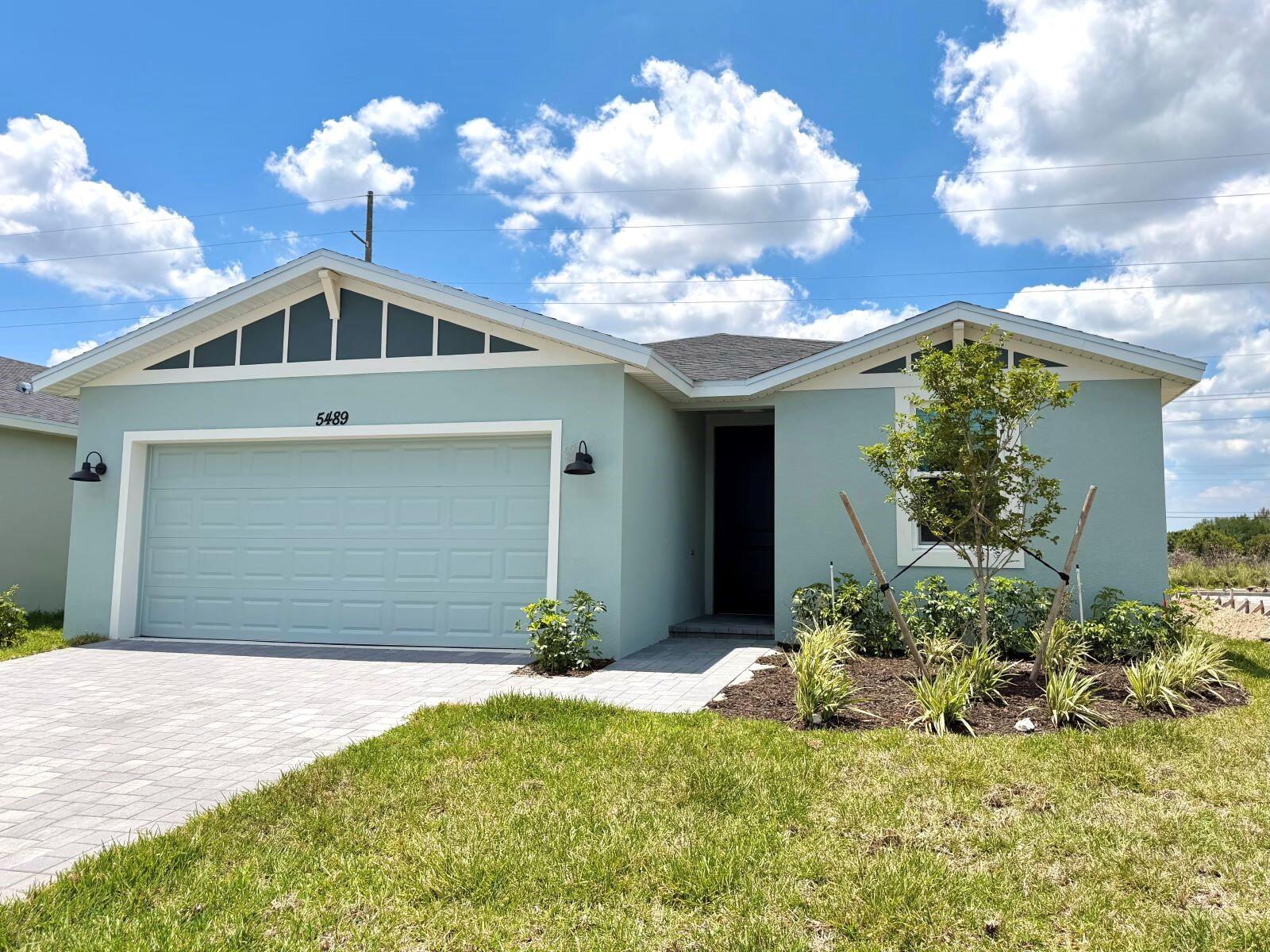 A light blue single-story house features a two-car garage and a landscaped front yard — 5489 Hampton Park Circle, Vero Beach FL 32966, VERO BEACH, FL