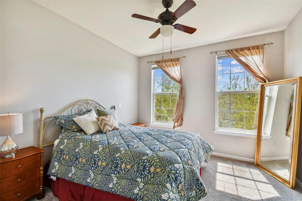 A bedroom features a bed with a floral quilt, two windows, and a floor mirror — 4221 W SPRUCE STREET UNIT 2323, TAMPA, FL