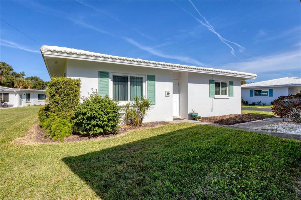 A white single-story house features green shutters, a white roof, and a grassy front yard — 1815 ROXANE WAY UNIT 65, SARASOTA, FL