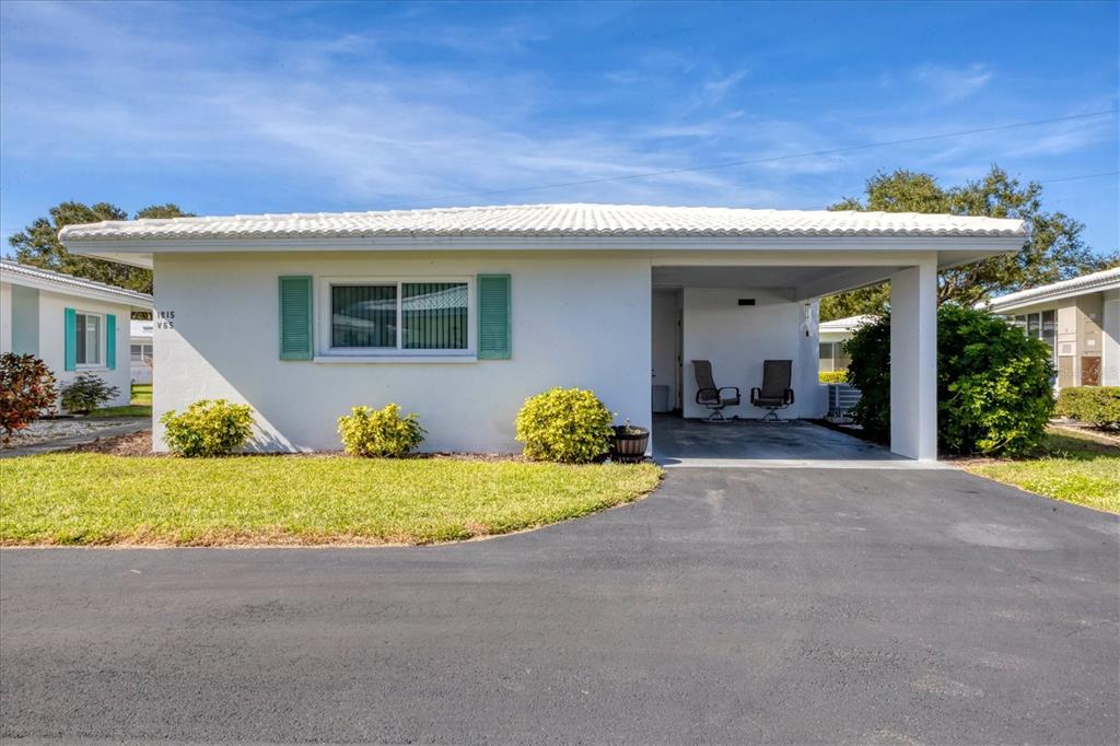 A white single-story house features a carport, green shutters, and a paved driveway — 1815 ROXANE WAY UNIT 65, SARASOTA, FL
