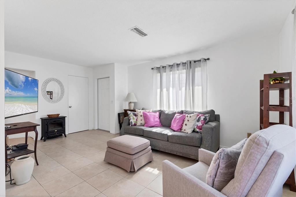 A living room features a grey sofa, an ottoman, a television, and light-colored tile flooring — 1815 ROXANE WAY UNIT 65, SARASOTA, FL