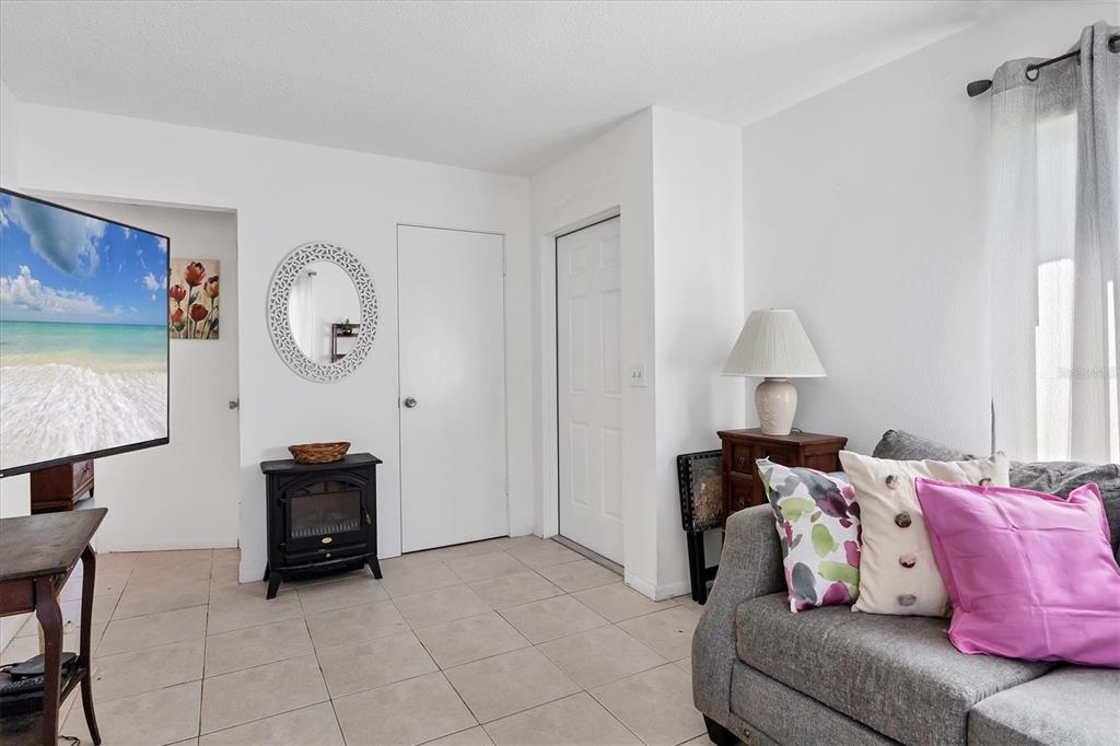 A living room features tile flooring, a grey sofa, a television, and a small fireplace — 1815 ROXANE WAY UNIT 65, SARASOTA, FL