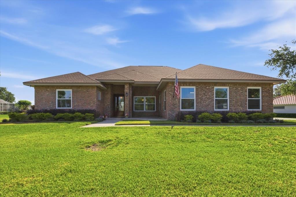 A single-story brick house with a hip roof and a front lawn under a blue sky — 17825 SIMMS ROAD, ODESSA, FL
