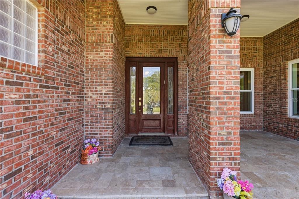 A brick-faced home entrance features a wooden front door with glass panels and stone flooring — 17825 SIMMS ROAD, ODESSA, FL
