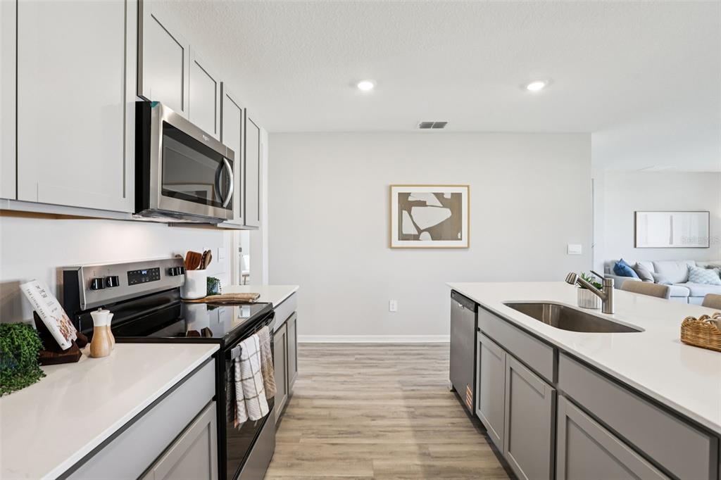 A modern kitchen features gray cabinets, white countertops, stainless steel appliances, and wood-look flooring — 7834 FORREST FOX WAY, LAKELAND, FL