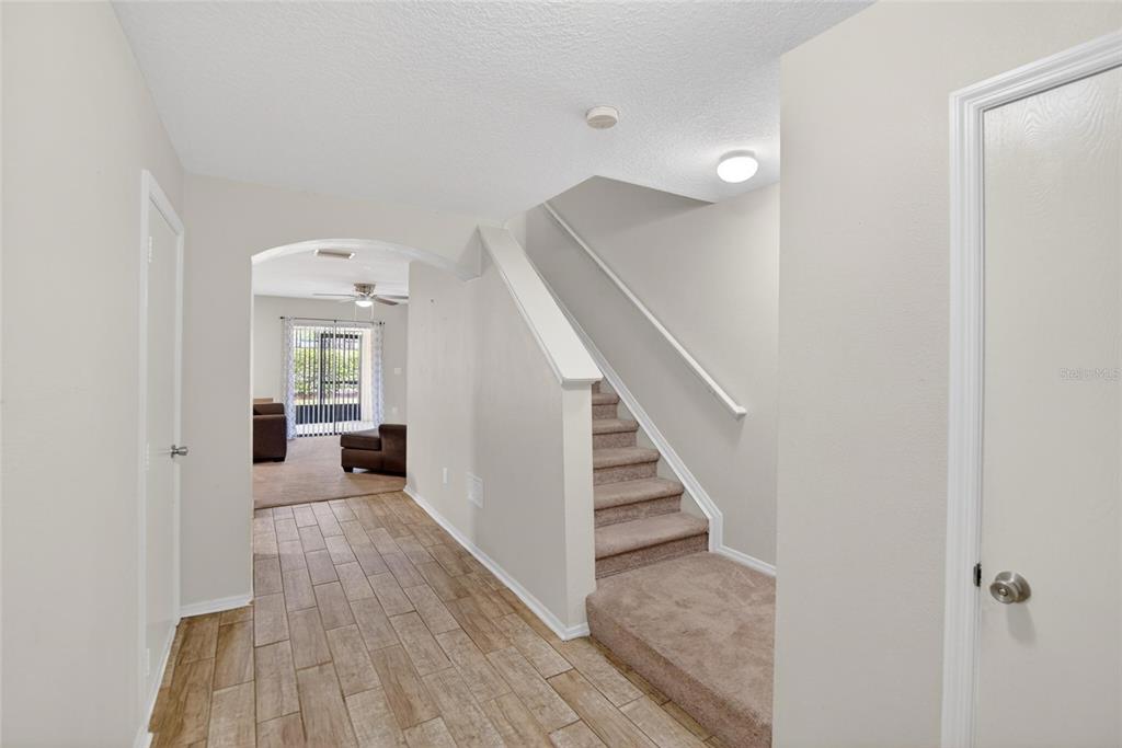 A hallway with tile flooring leads to a living area past a carpeted staircase — 2605 OLEANDER LAKES DRIVE, BRANDON, FL