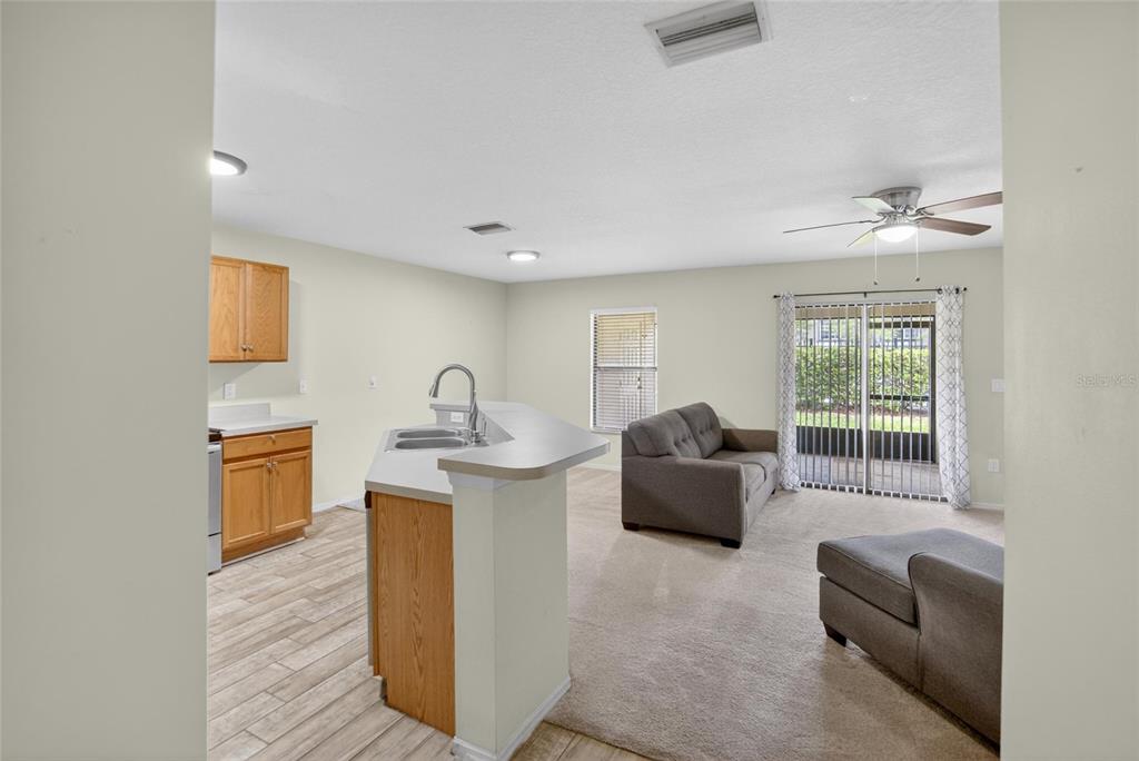 A kitchen with wood cabinets and a breakfast bar opens into a carpeted living area — 2605 OLEANDER LAKES DRIVE, BRANDON, FL
