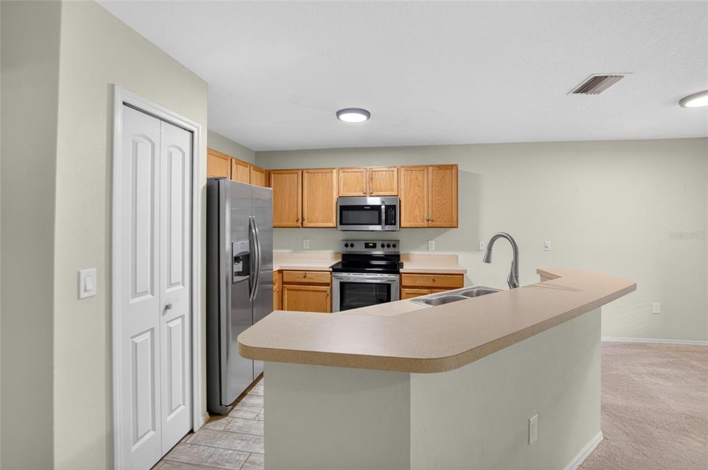 A kitchen features wood cabinets, stainless steel appliances, and a breakfast bar with laminate countertops — 2605 OLEANDER LAKES DRIVE, BRANDON, FL