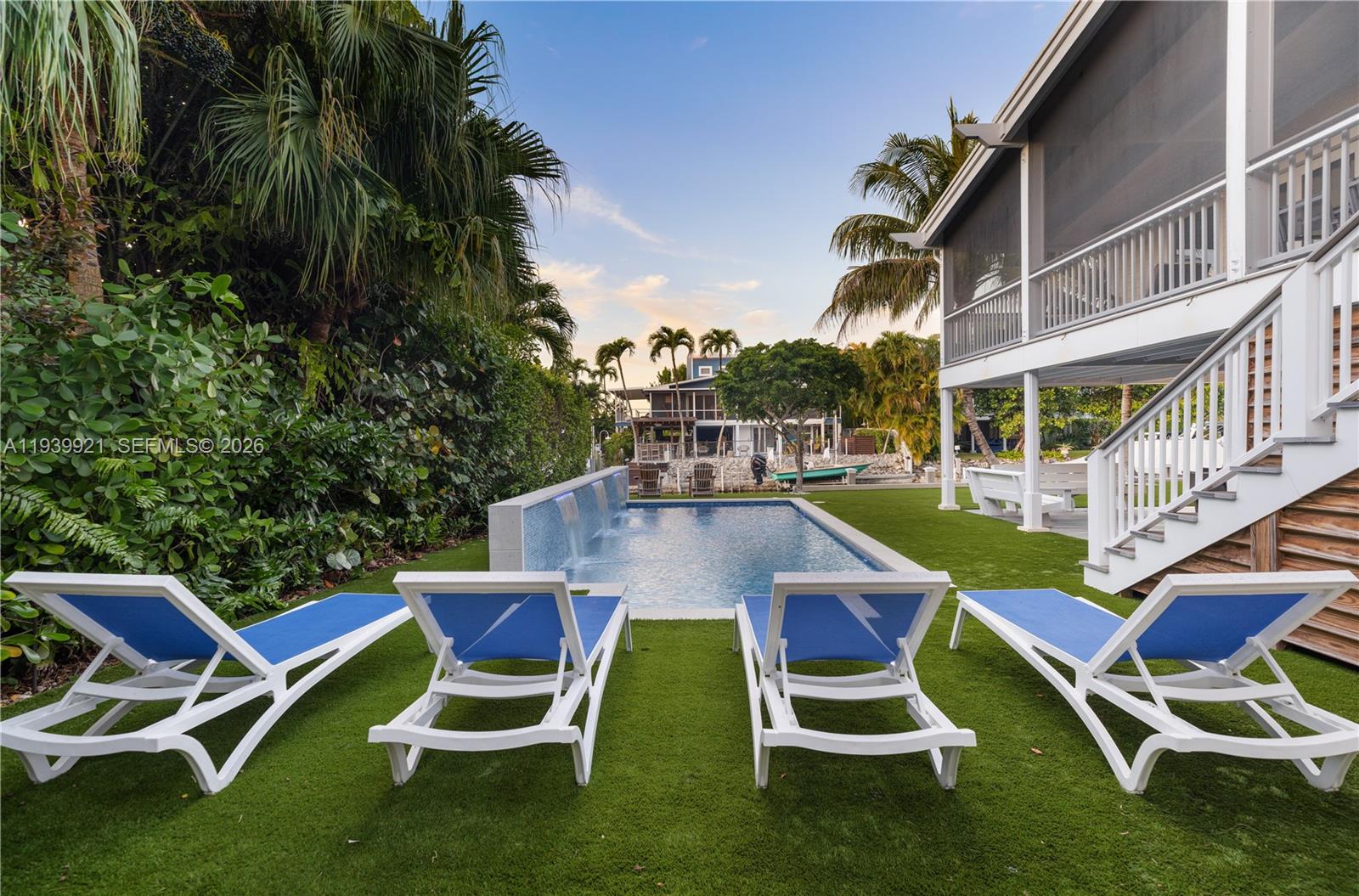 Four lounge chairs sit on artificial turf beside a rectangular swimming pool with a waterfall — 150 Rushton Ln, Tavernier FL 33070, TAVERNIER, FL